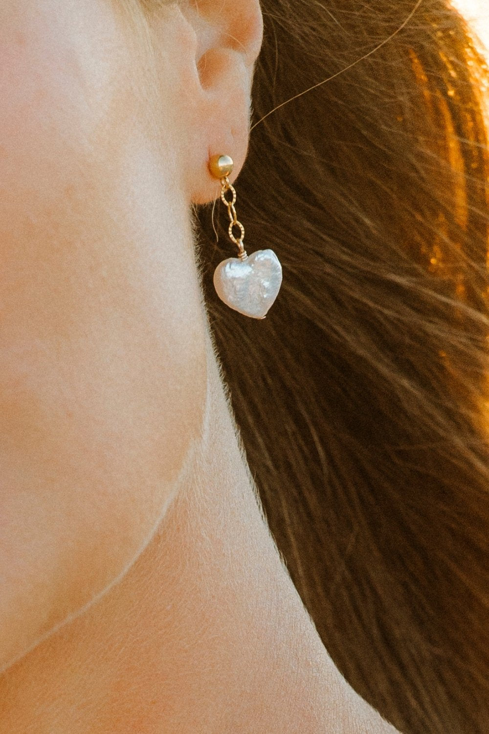 Close-up of a person wearing a heart-shaped pearl earring with gold chain.