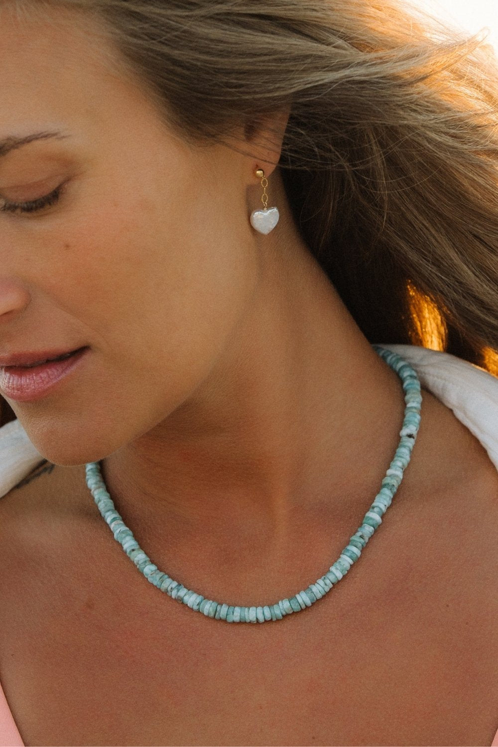 Close-up of a woman wearing a larimar beaded necklace and heart-shaped amor earrings.