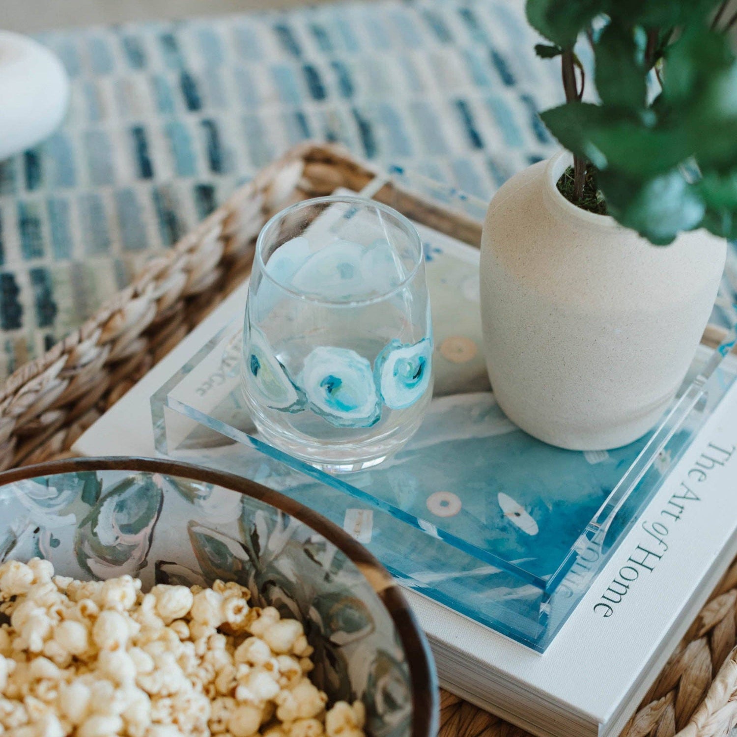 Tray with popcorn, glass, book, and plant on a textured surface