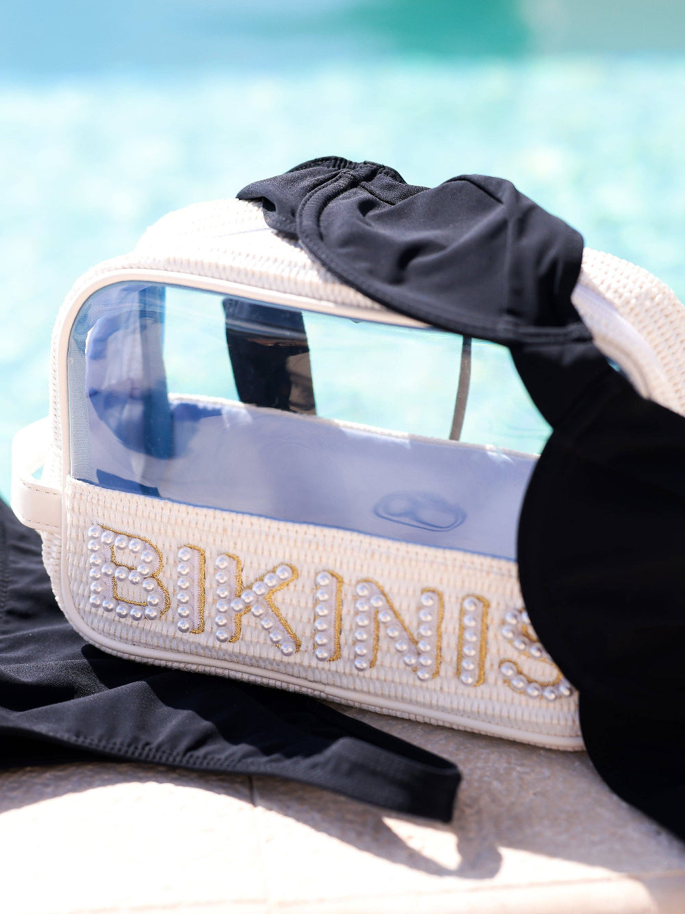 Beige bag with 'BIKINIS' text and black swimsuit on a blurred background