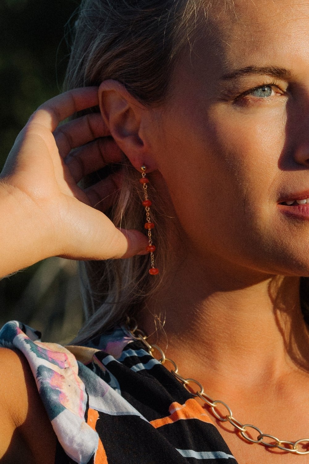 Close-up of a woman wearing carnelian clementine earrings with a blurred background