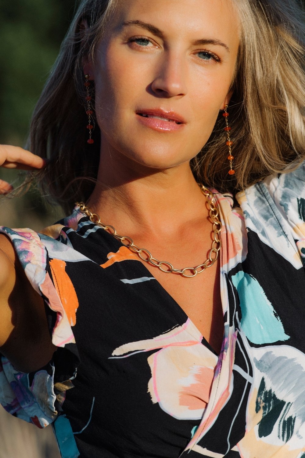 Woman wearing carnelian clementine earrings and a gold mattie chain necklace