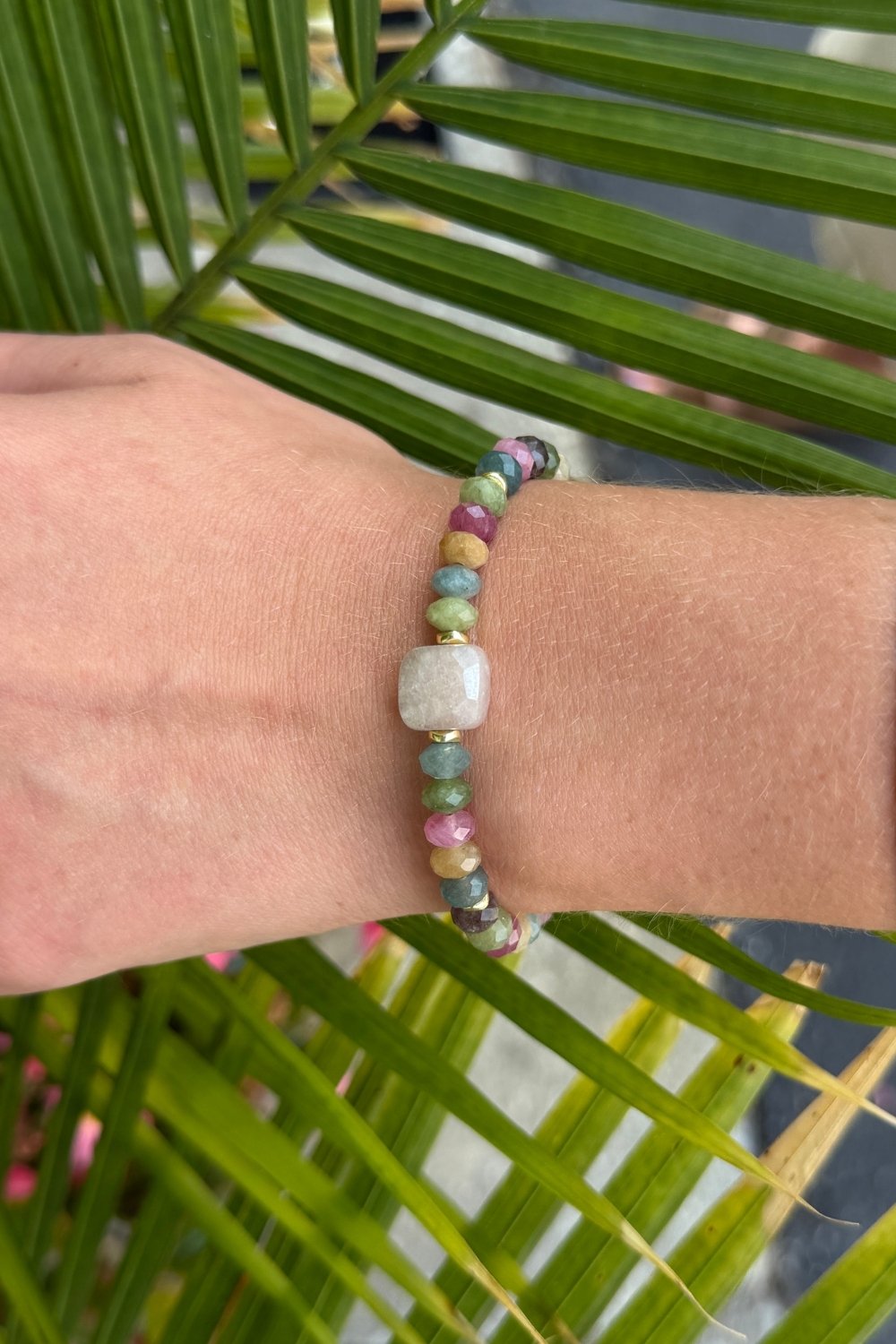Close-up of a wrist wearing a beaded Catalina bracelet with a palm leaf background