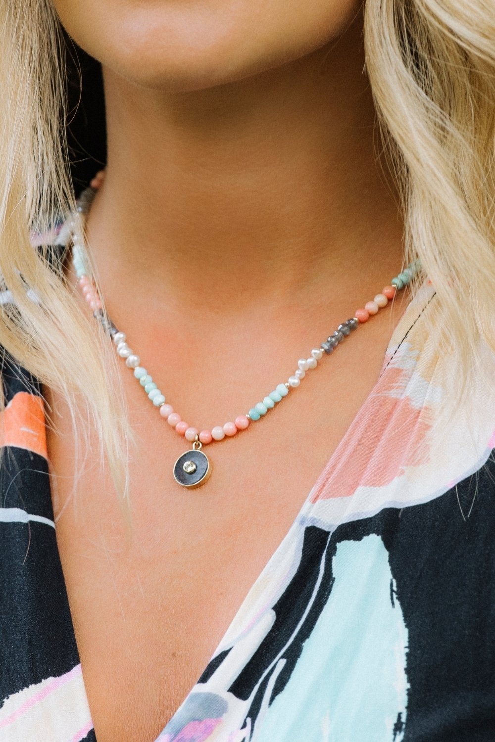 coral cove Necklace with colorful beads and a dark pendant worn by a person with blonde hair.