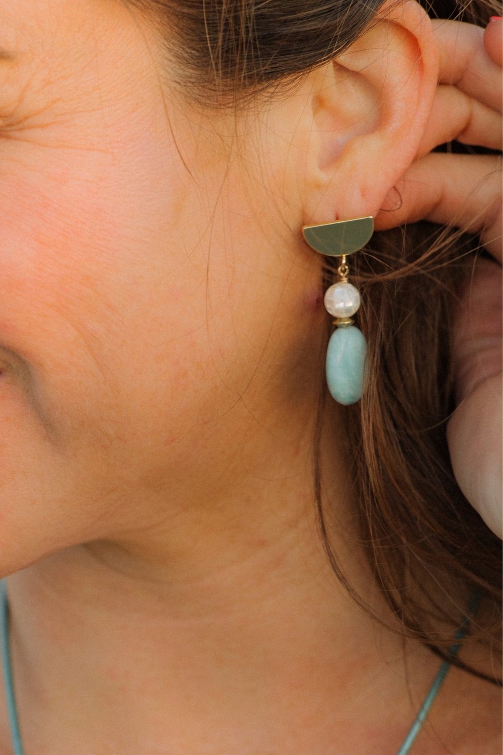 Close-up of Crescent tide earring with mother of pearl and an amazonite gemstone worn by a person.