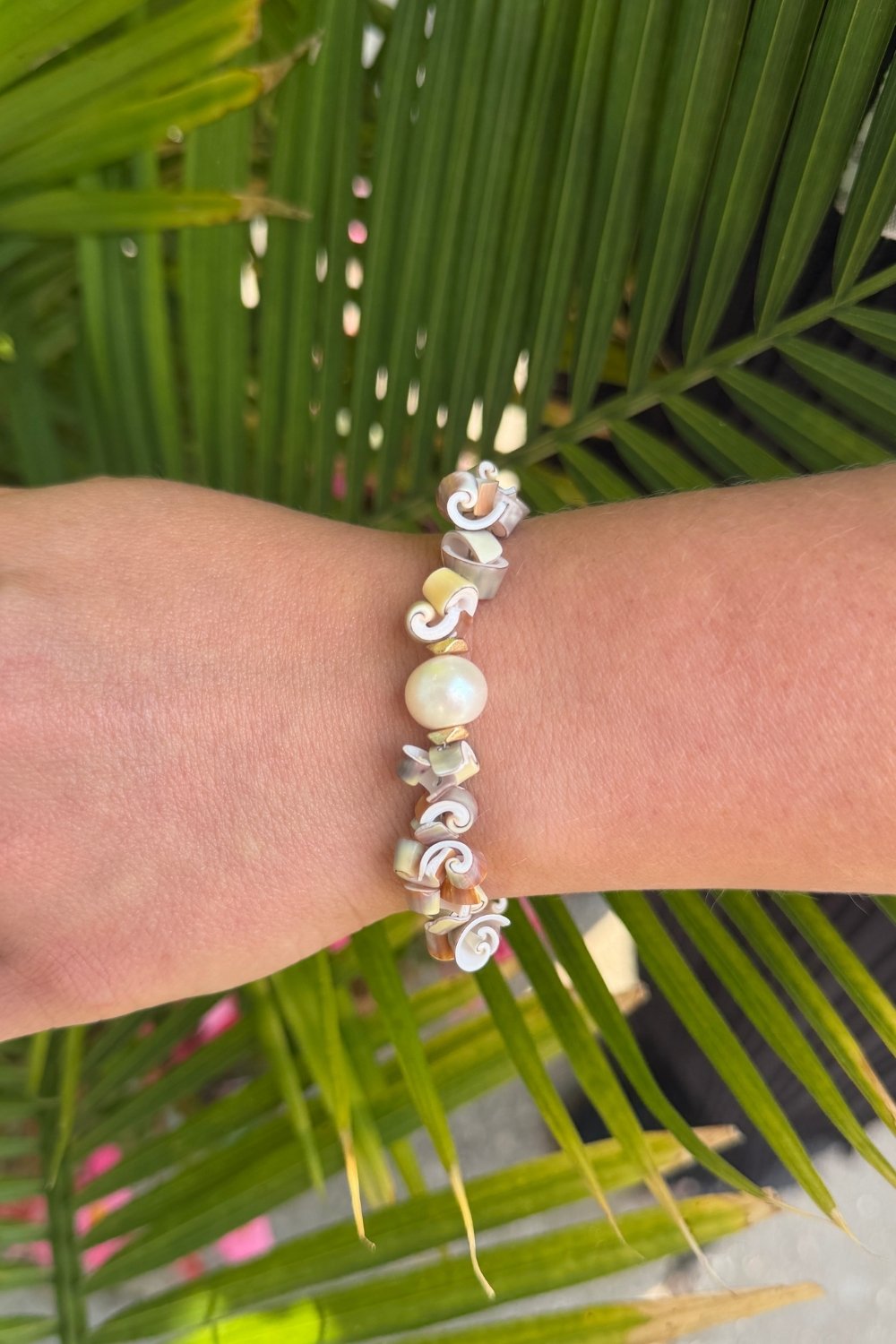 Deewees shell bracelet on a wrist with a palm leaf background