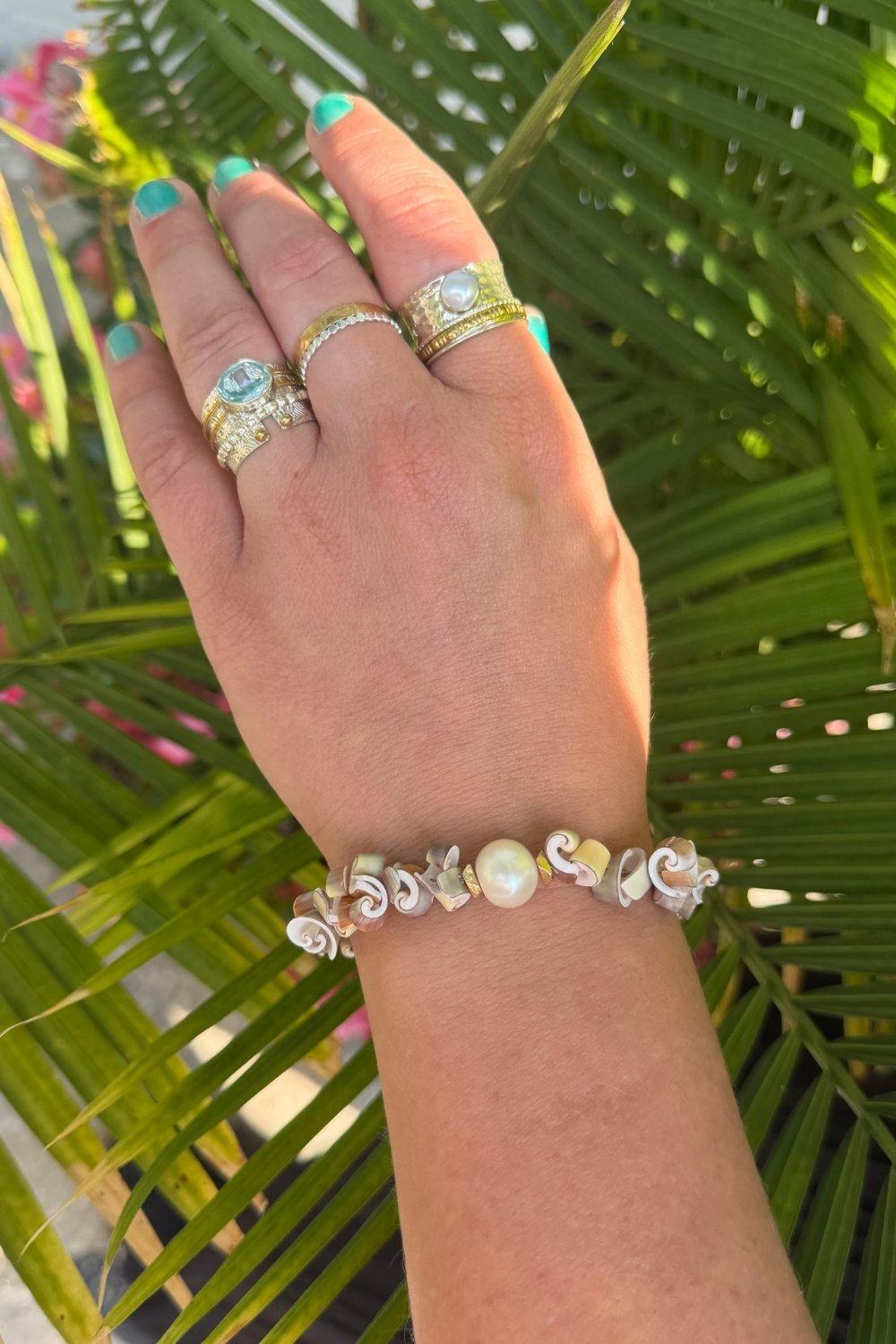 Hand wearing multiple rings and a Deewees bracelet with green leafy background