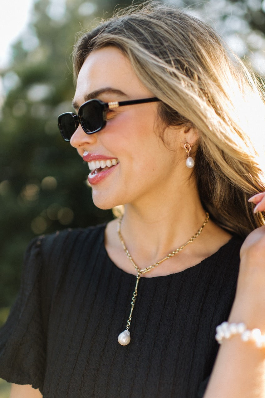 Woman wearing sunglasses and a black top with a blurred outdoor background