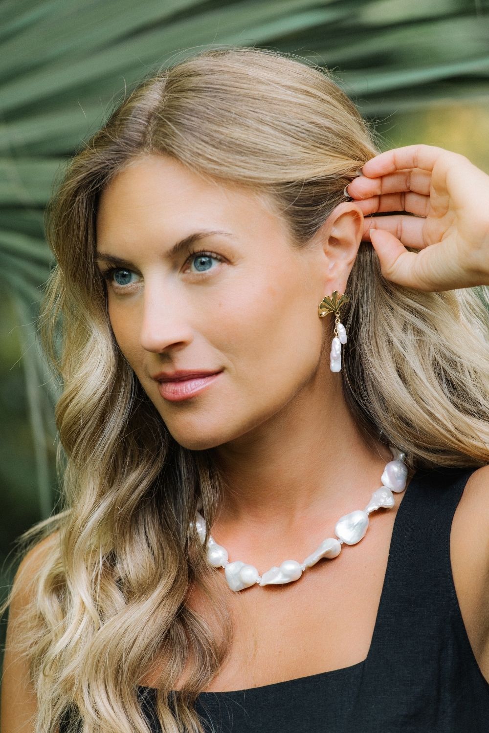 Woman wearing an heirloom pearl necklace and gingko glimmer earrings with a blurred green background