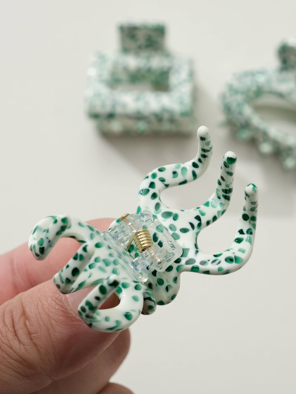 Green and white polka dot hair clip held by a hand with more hair clips in the background.