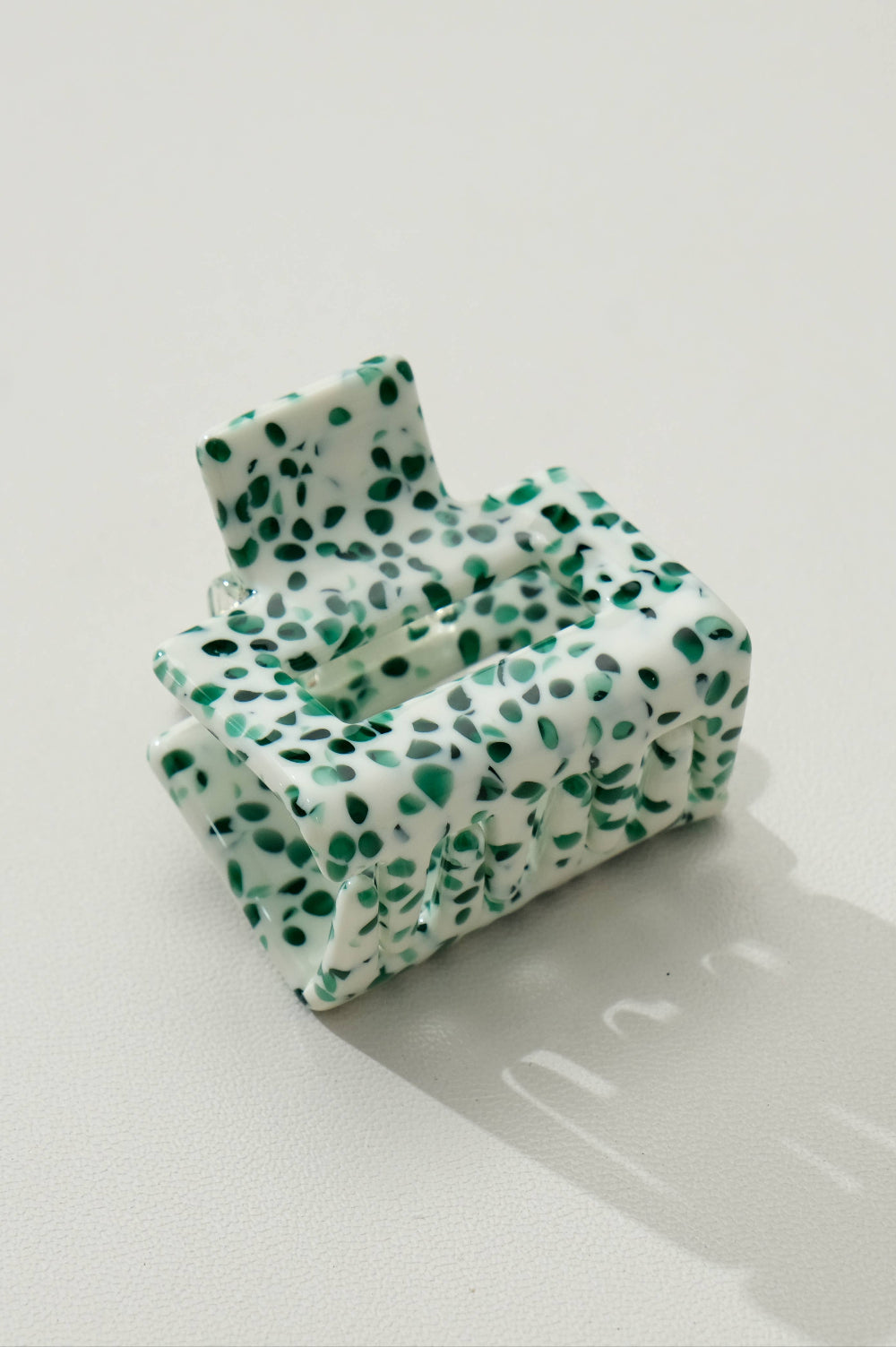 Green and white patterned hair clip on a light gray surface