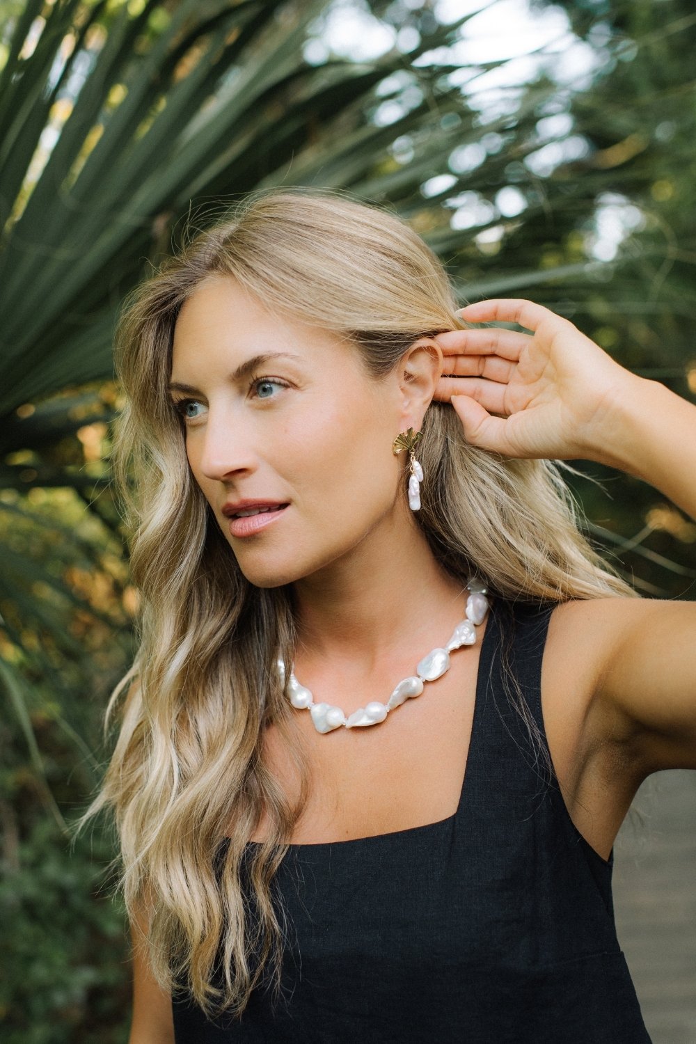 Woman showing off heirloom pearl necklace and gingko glimmer earrings