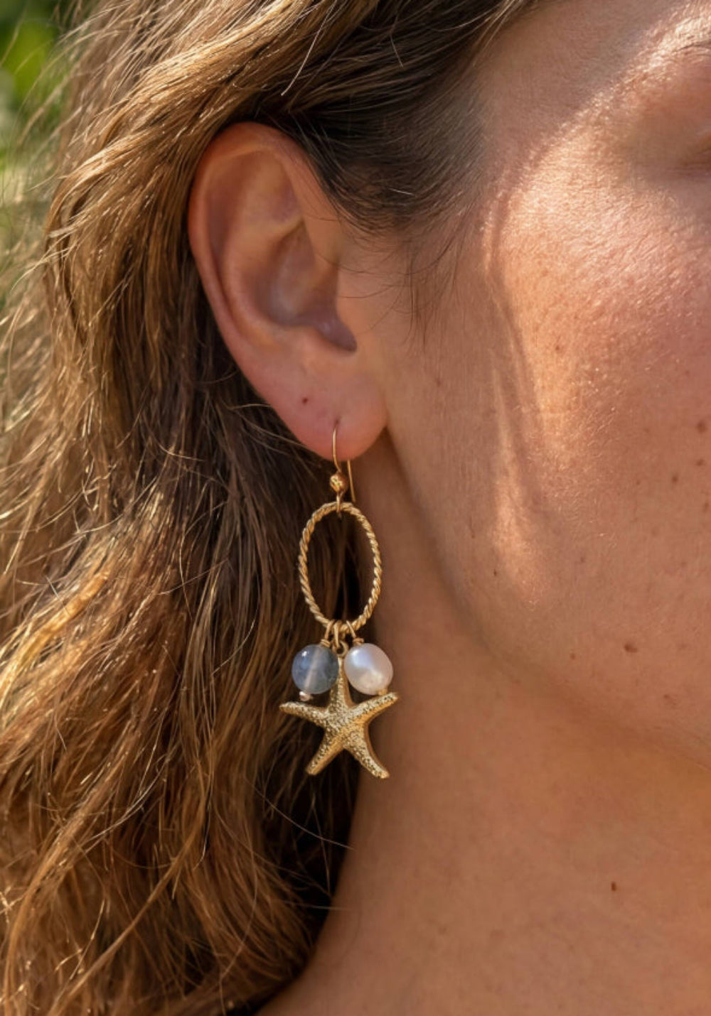 Woman wearing gold earrings with starfish and pearl design outdoors