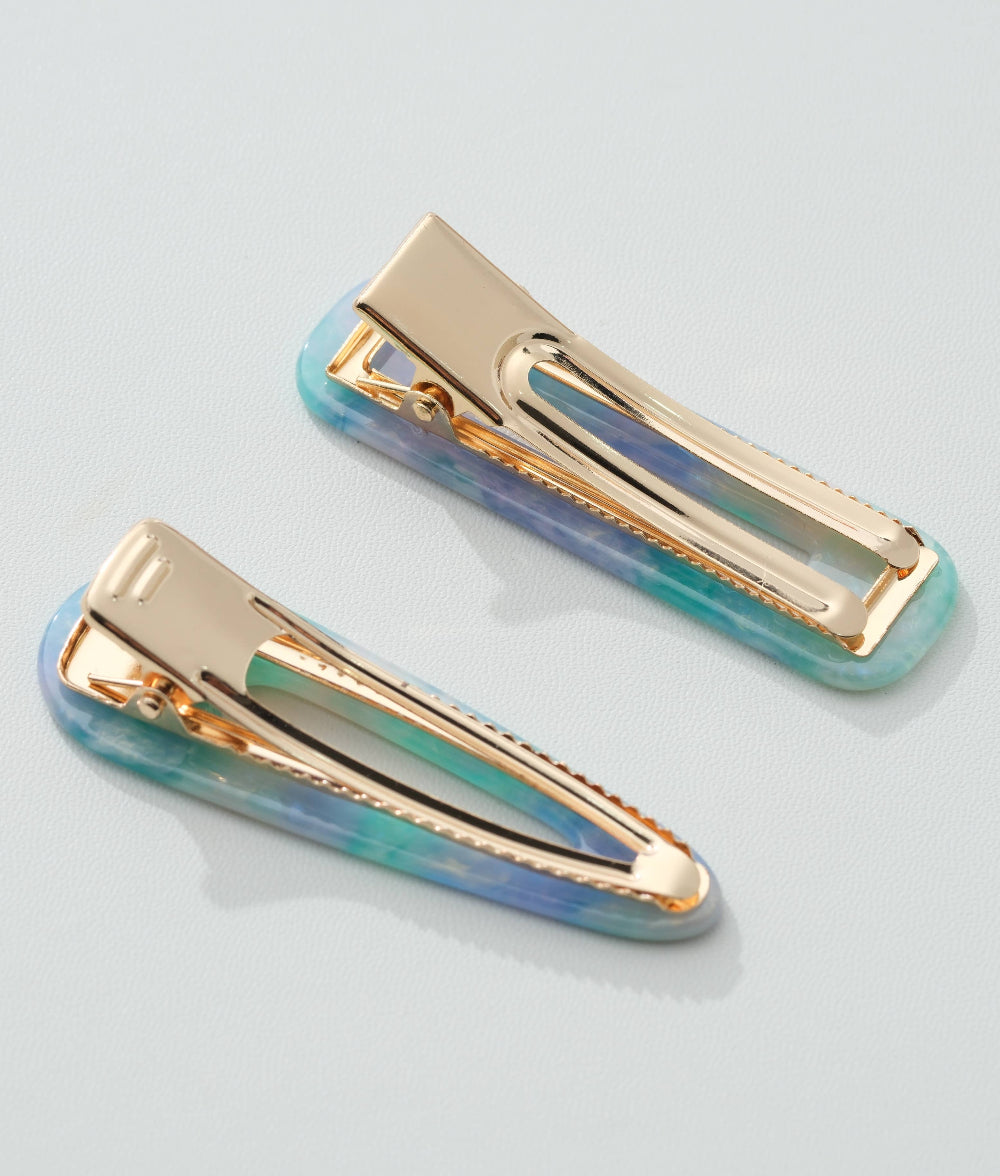 Two gold hair clips with iridescent blue and green design on a light gray background