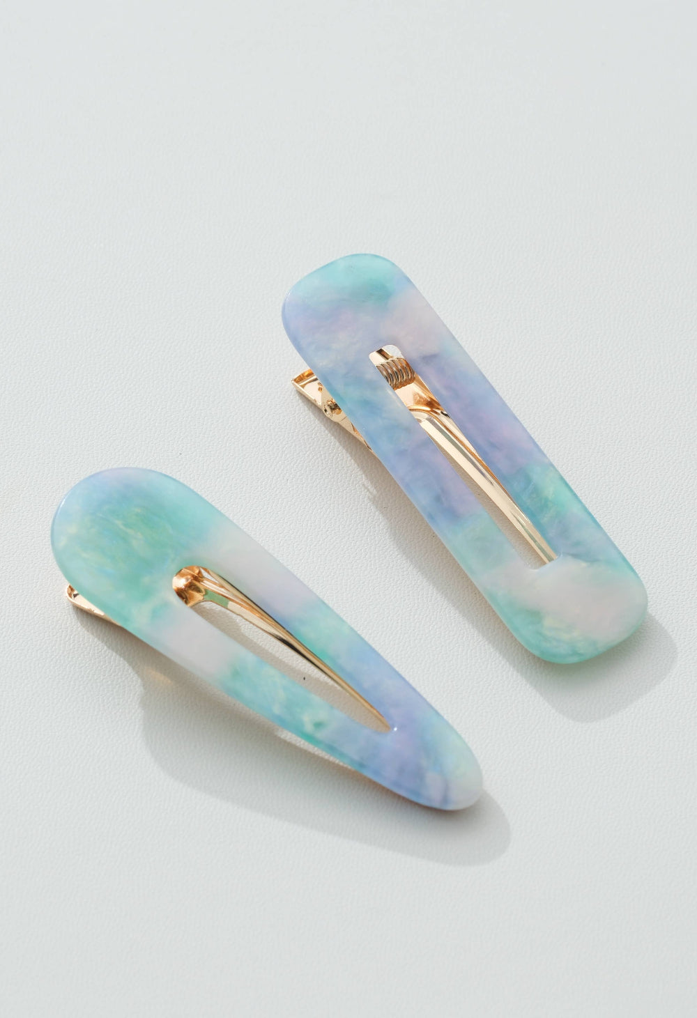Two pastel-colored hair clips with gold hardware on a light gray background