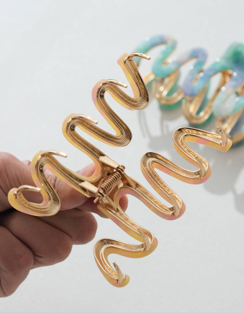 Gold spiral hair clip held by a hand with additional clips in the background on a light surface.