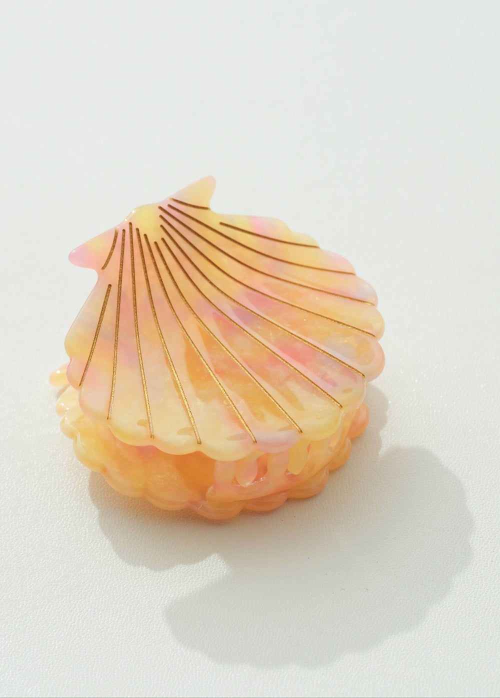 Shell-shaped claw clip with a gradient of pink to yellow on a white background
