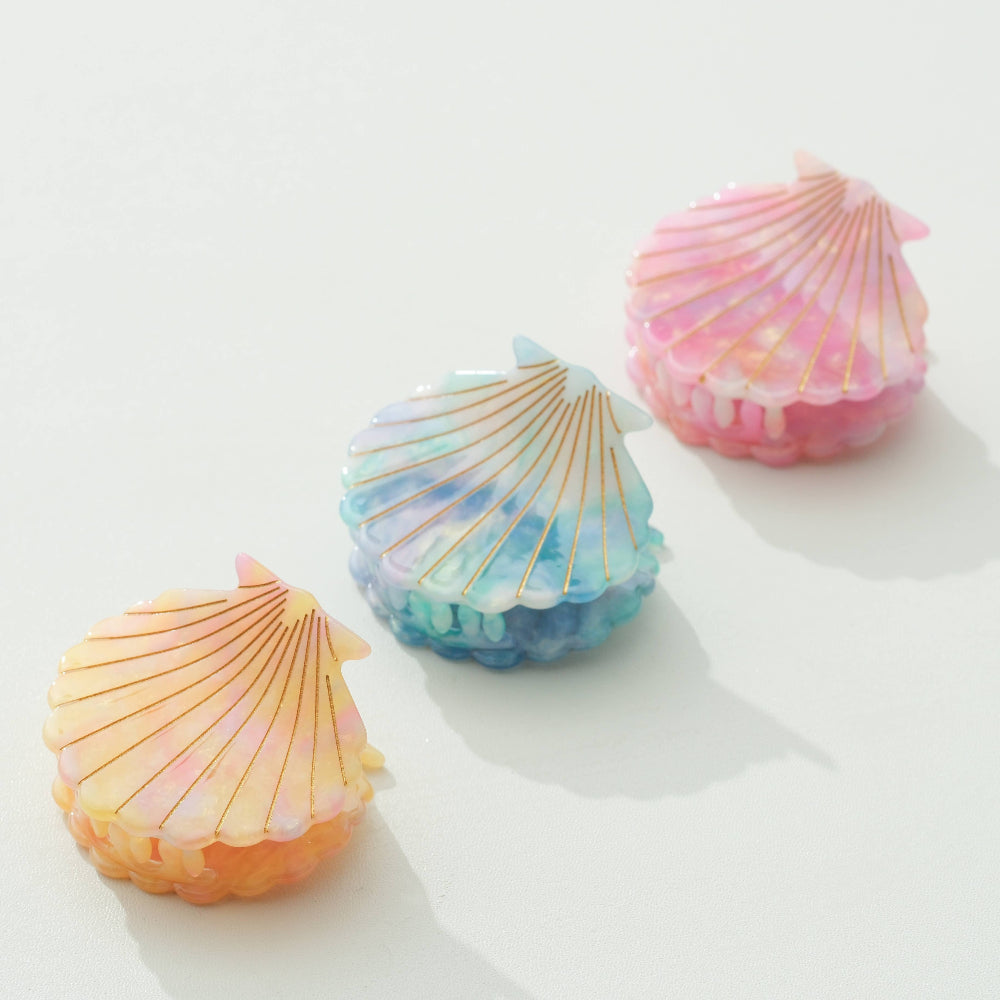 Three shell-shaped claw clips in pastel colors on a white surface