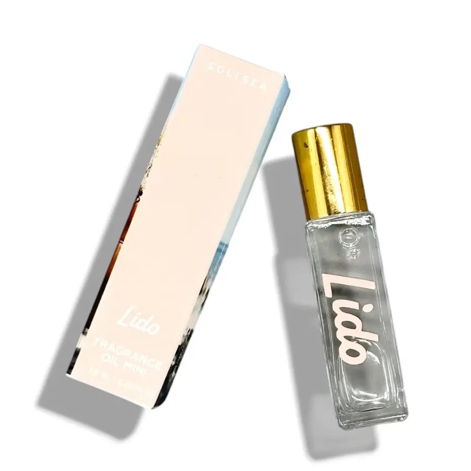 A clear glass perfume bottle with a shiny gold cap next to its pale pink and white box, both featuring the brand name 'Solisea' and product name 'Lido Fragrance Oil Mini'.