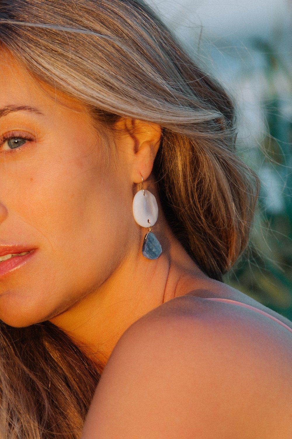 Close-up of a woman wearing the marina earrings with a blurred natural background
