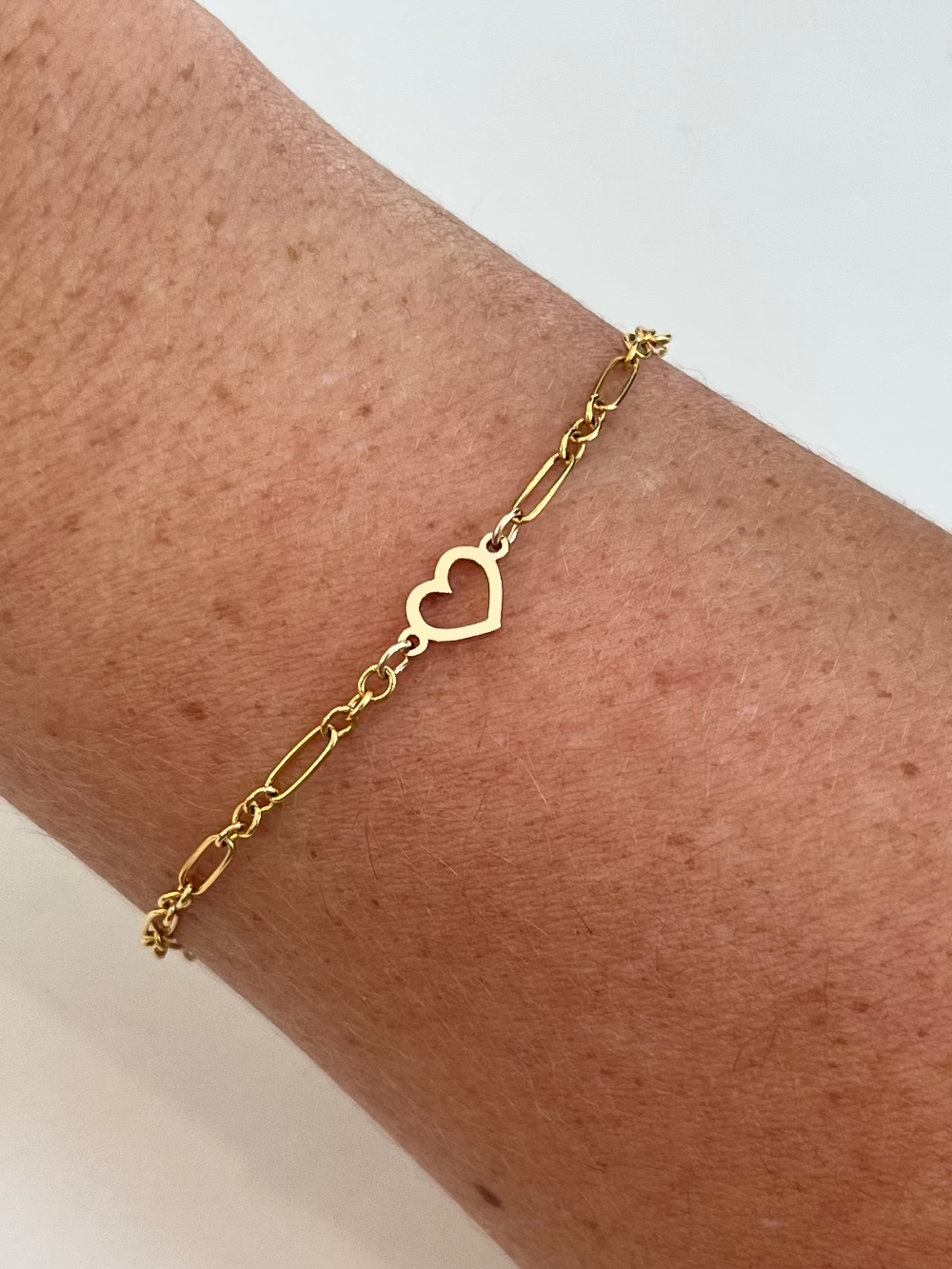 Gold bracelet with a heart charm on a wrist against a light background