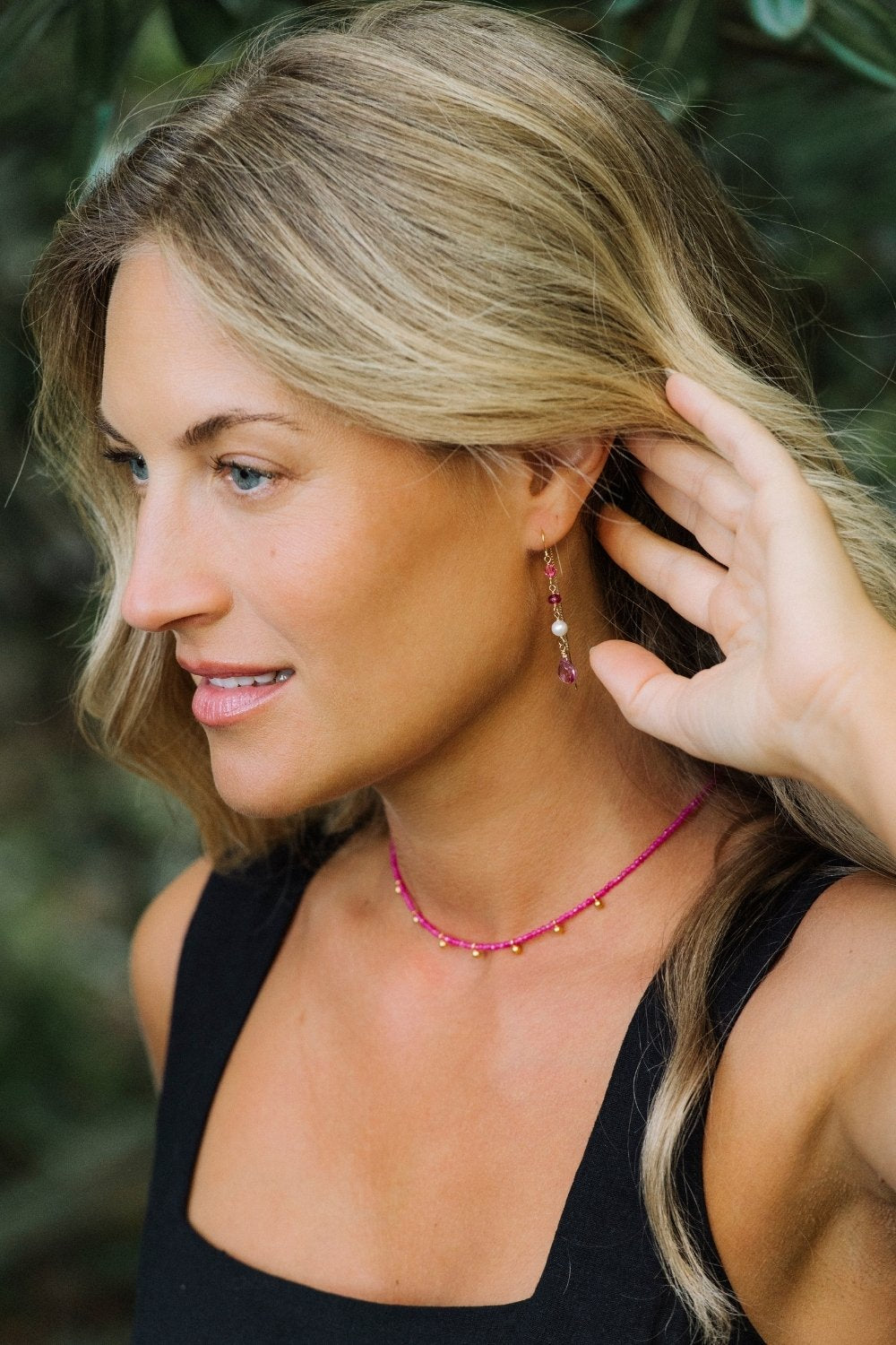 Woman adjusting a pink paloma earring with a blurred green background