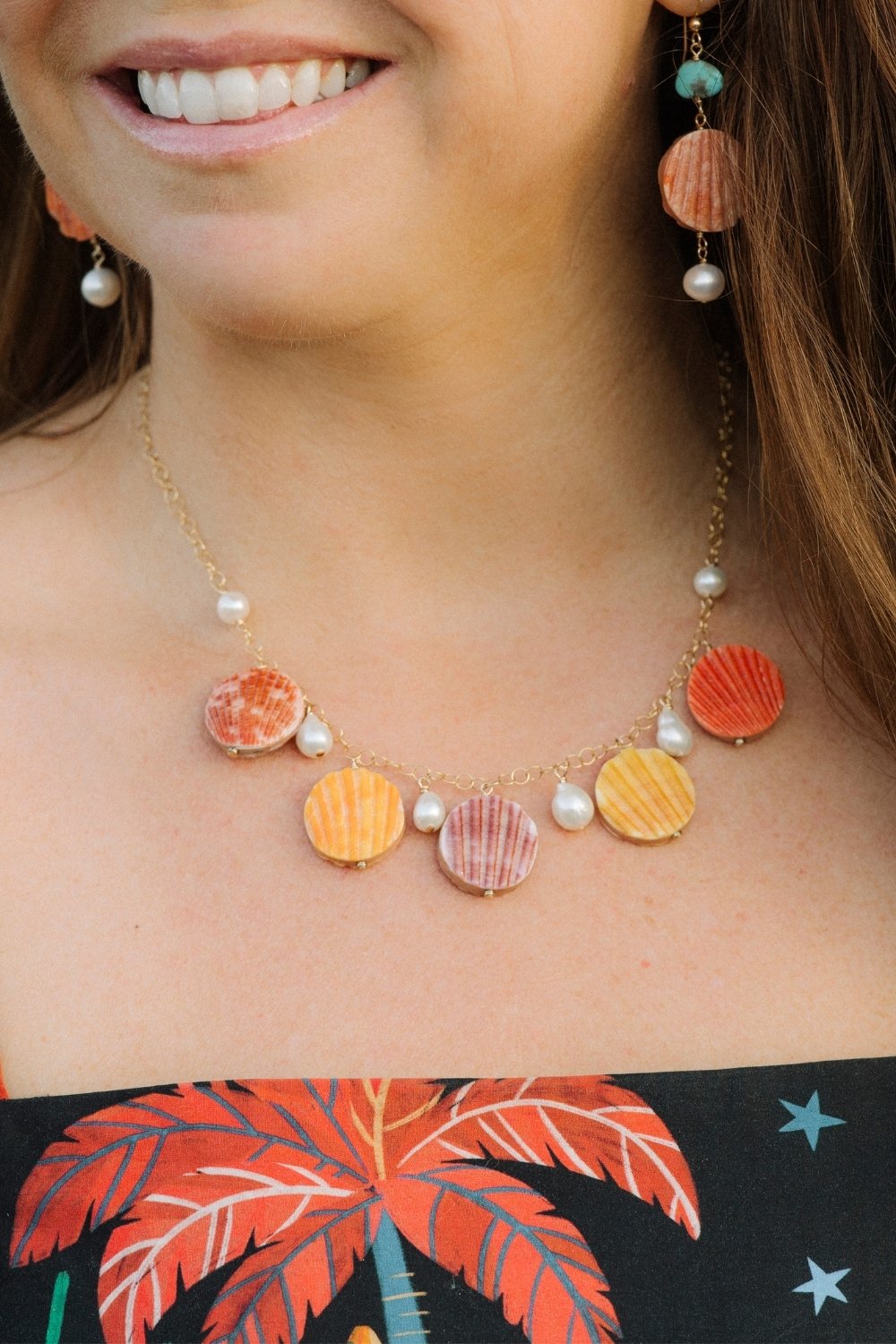 Close-up of a woman wearing a colorful Scallop Sunset necklace with shell pendants and pearl accents.