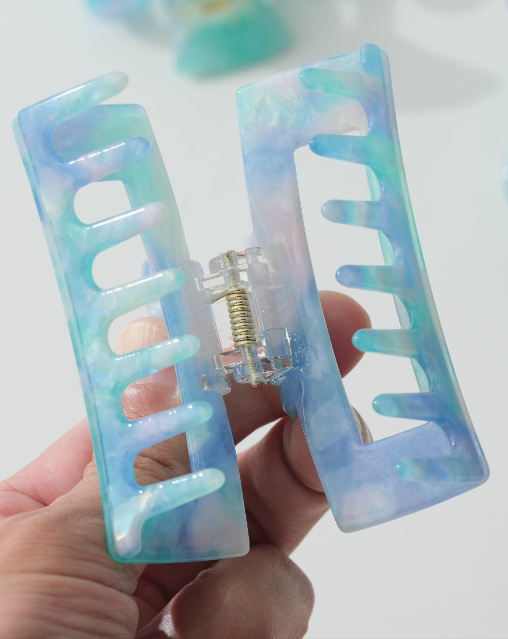 Iridescent hair clip held by a hand against a light background