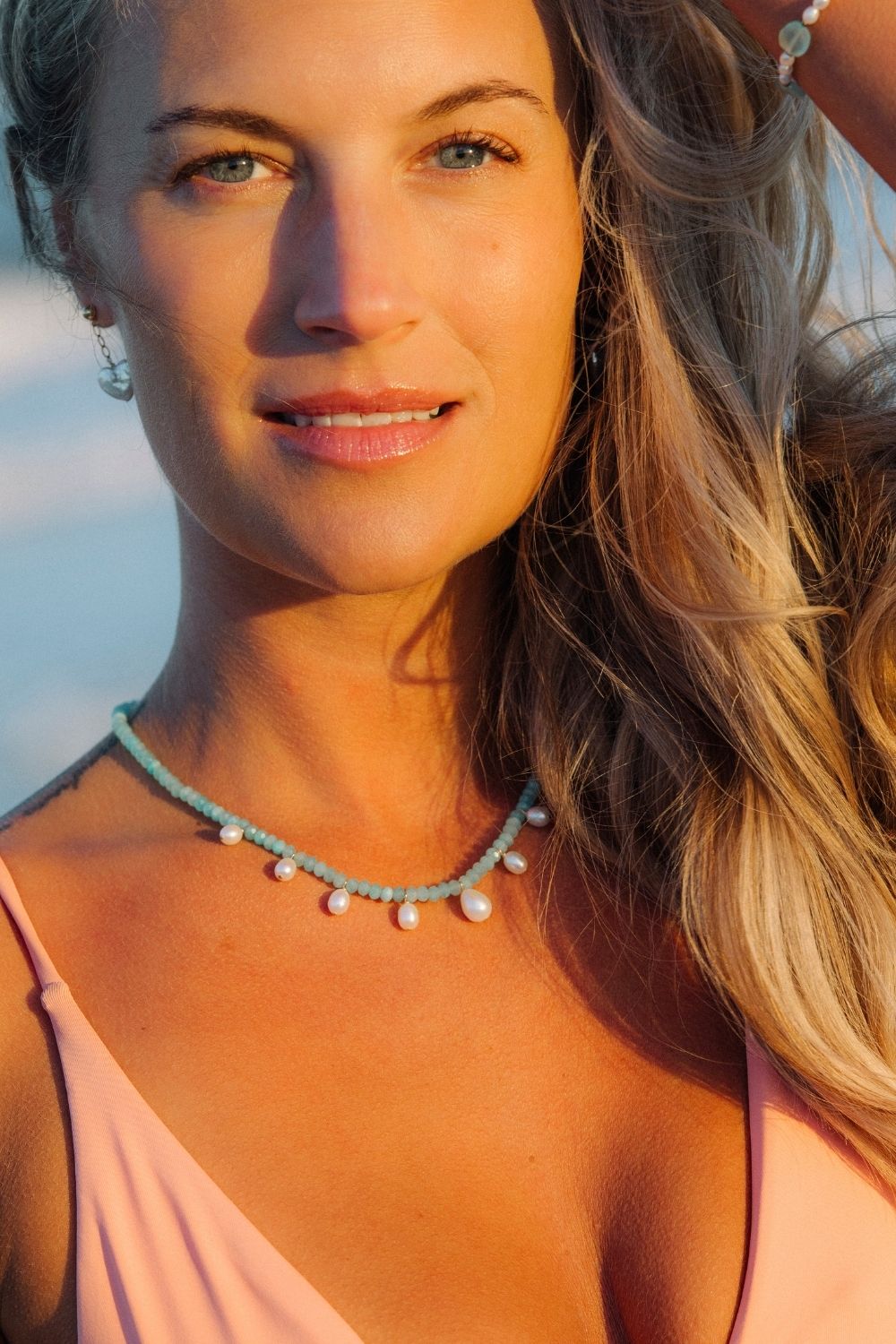 Woman wearing a seafoam pearl necklace with a blurred beach background