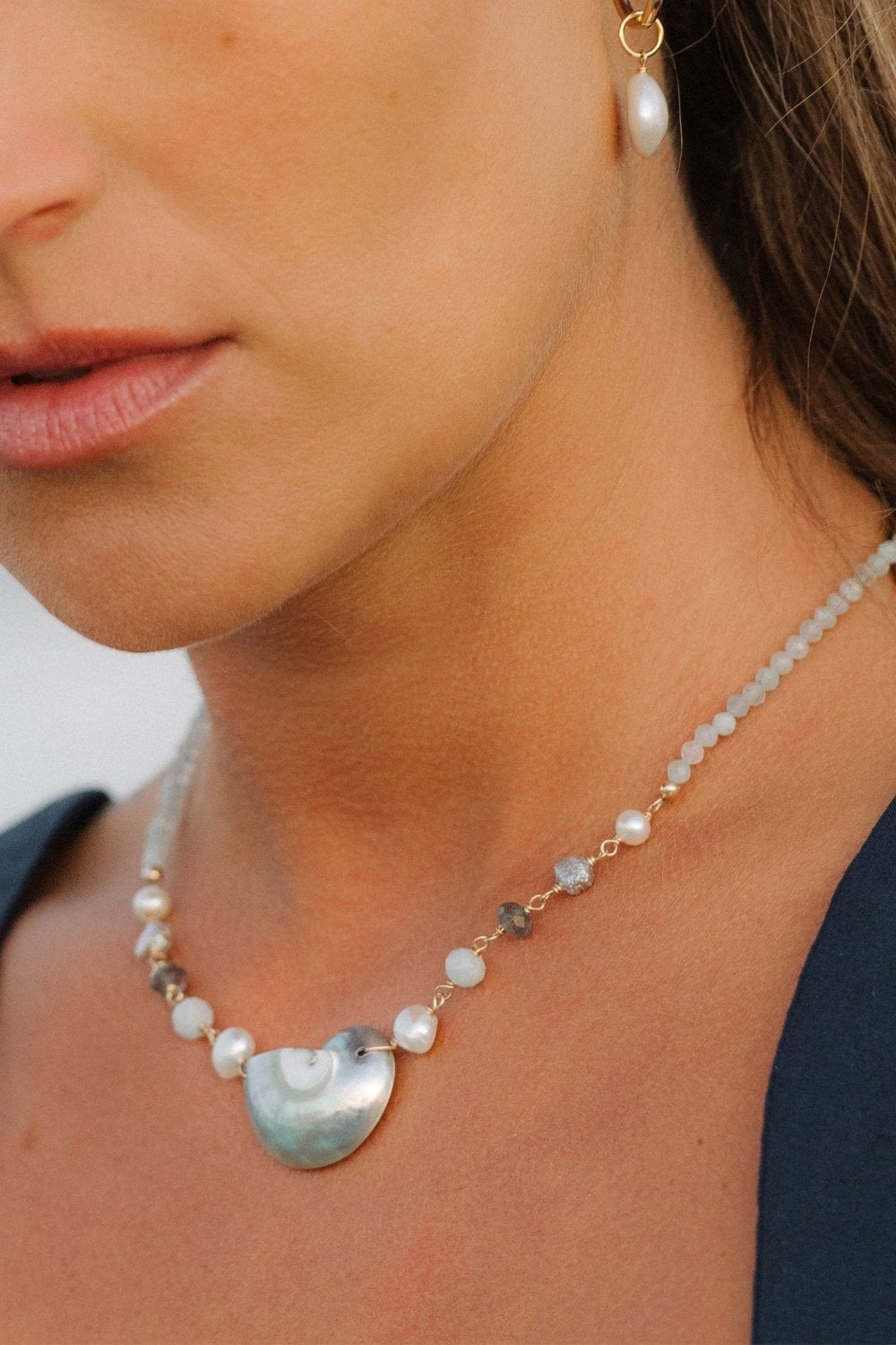 Close-up of a woman wearing a shoreline shell necklace and pearl earrings.
