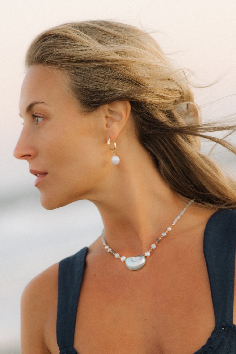 Woman wearing a shoreline shell necklace and pearl earrings with a blurred background