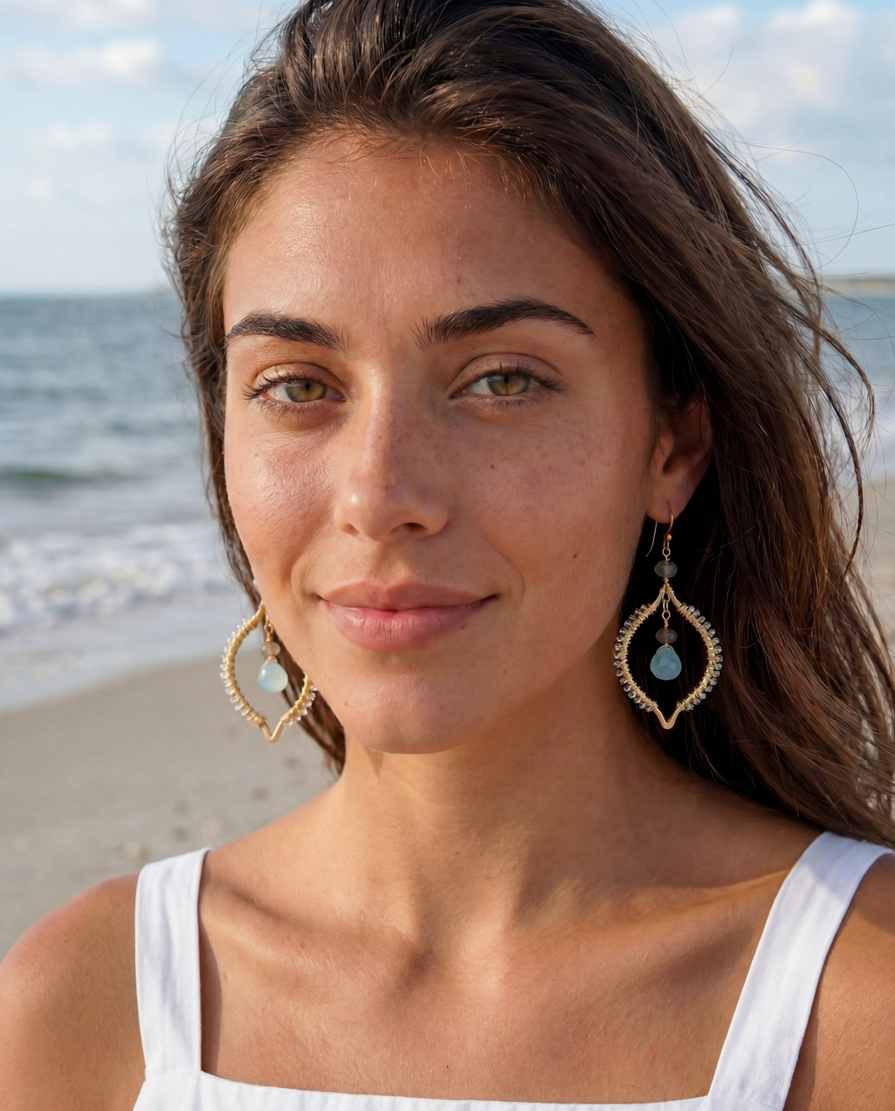 Woman on a beach wearing earrings with a scenic background