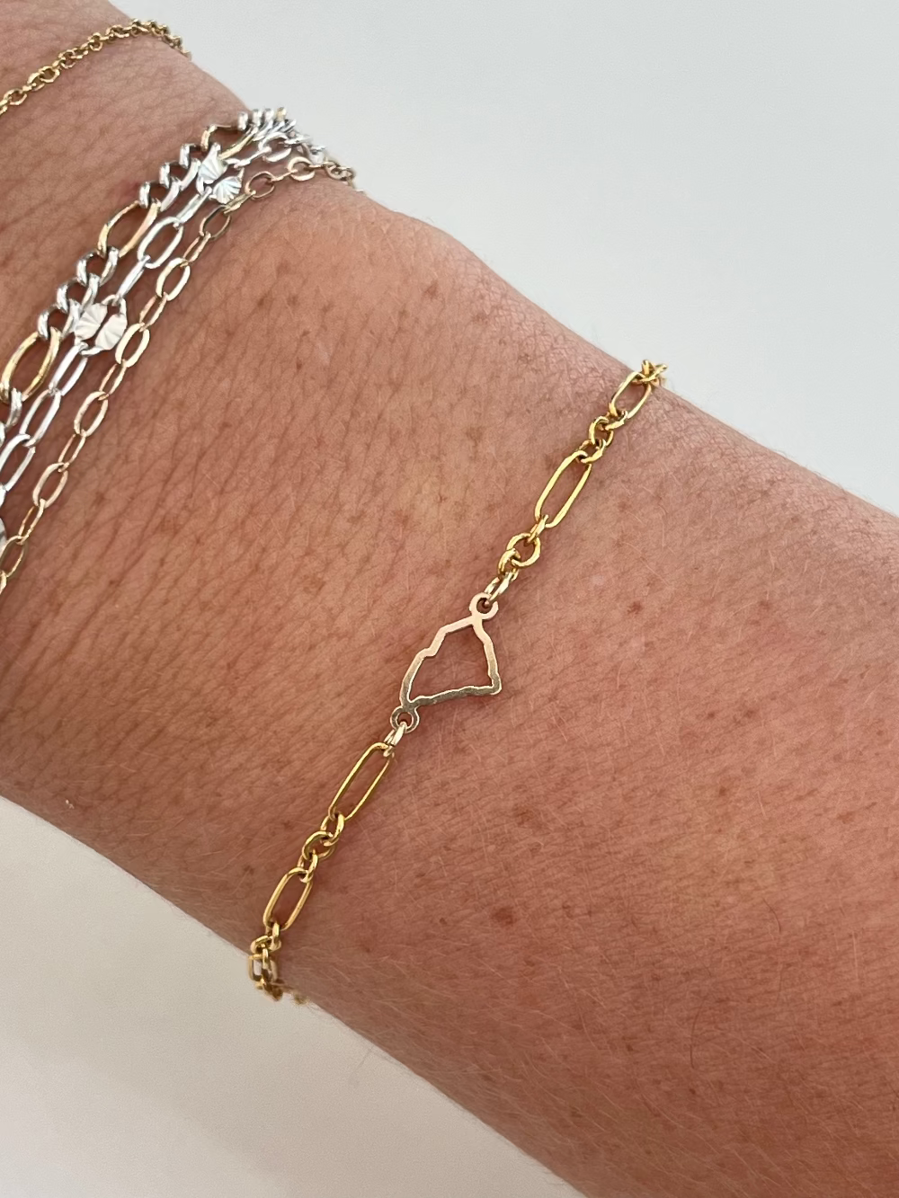 Gold chain bracelet on a wrist with a plain background