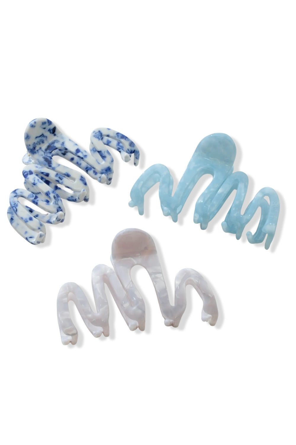 Three plastic claw hair clips in different colors and patterns: a blue and white marbled clip, a light blue solid clip, and a translucent white clip with a pinkish-tinted center, displayed on a clean white background.