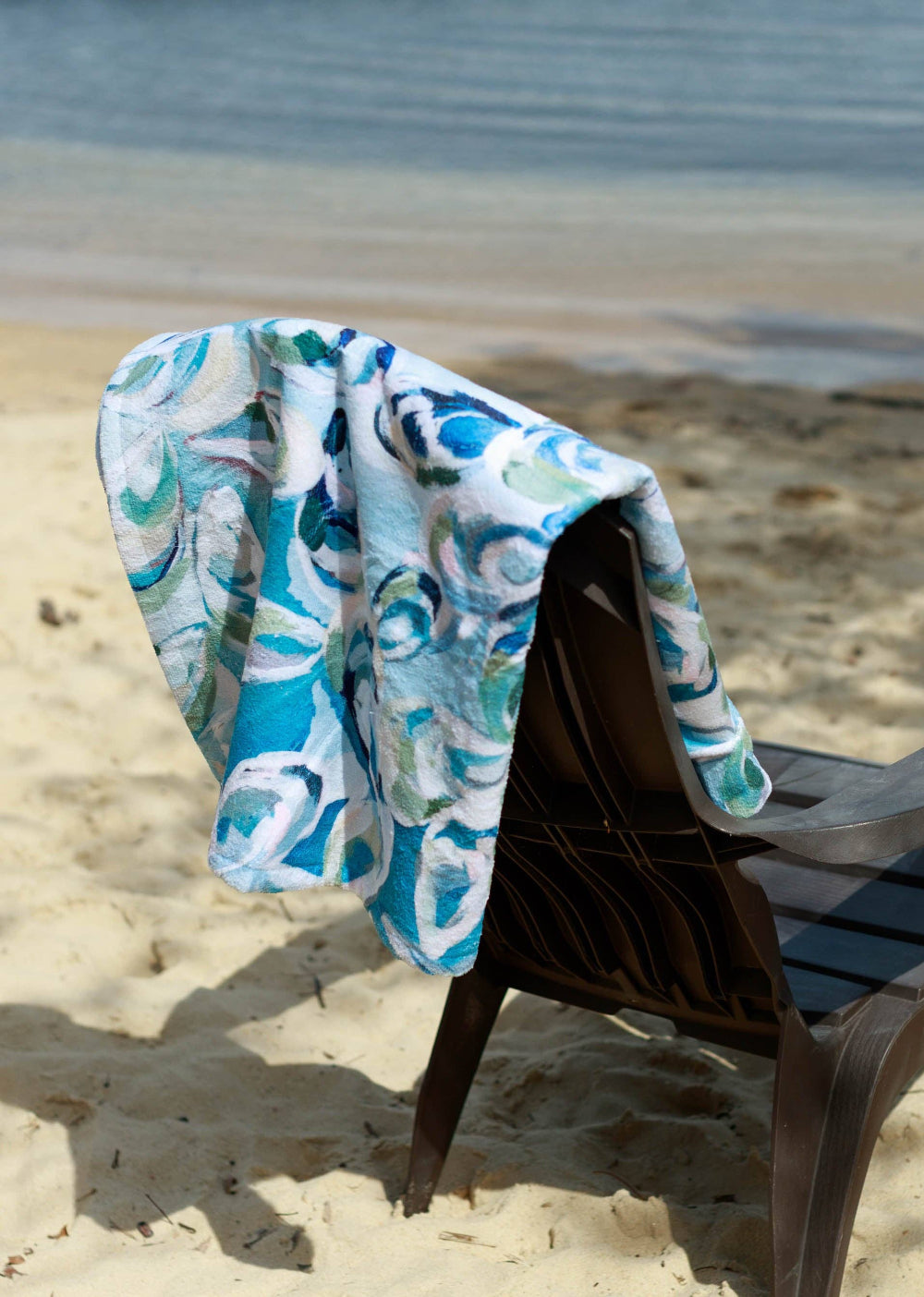 Beach chair with an oyster shell patterned towel draped over it on a sandy beach.