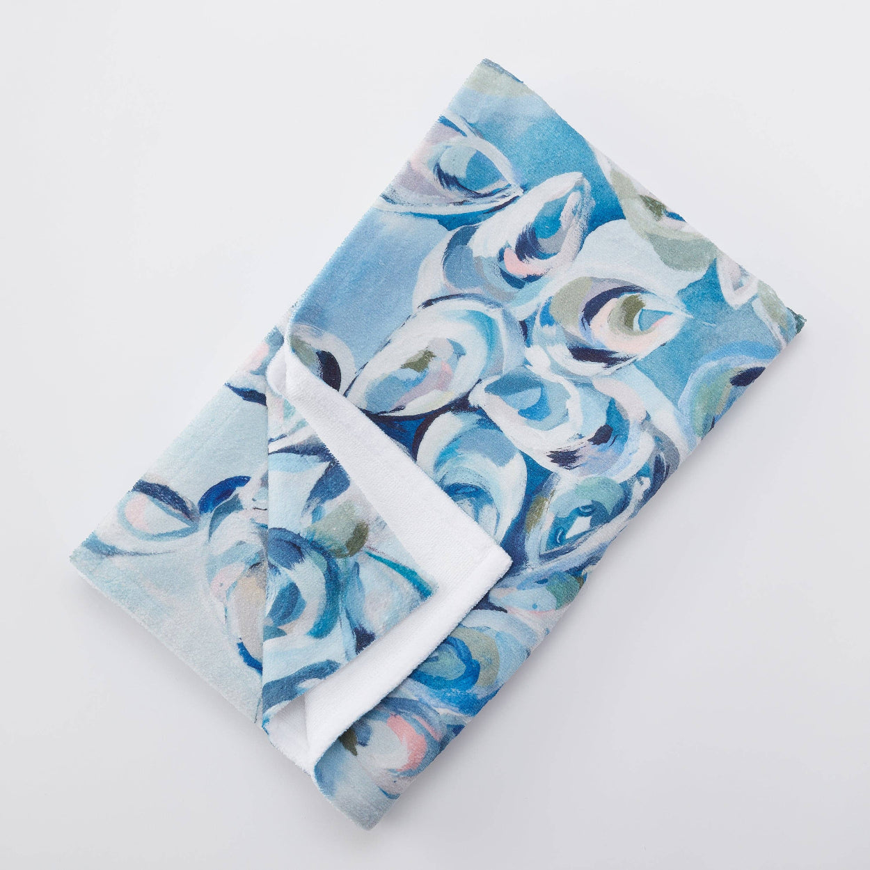Folded beach towel with blue and white oyster shell pattern on a light gray background