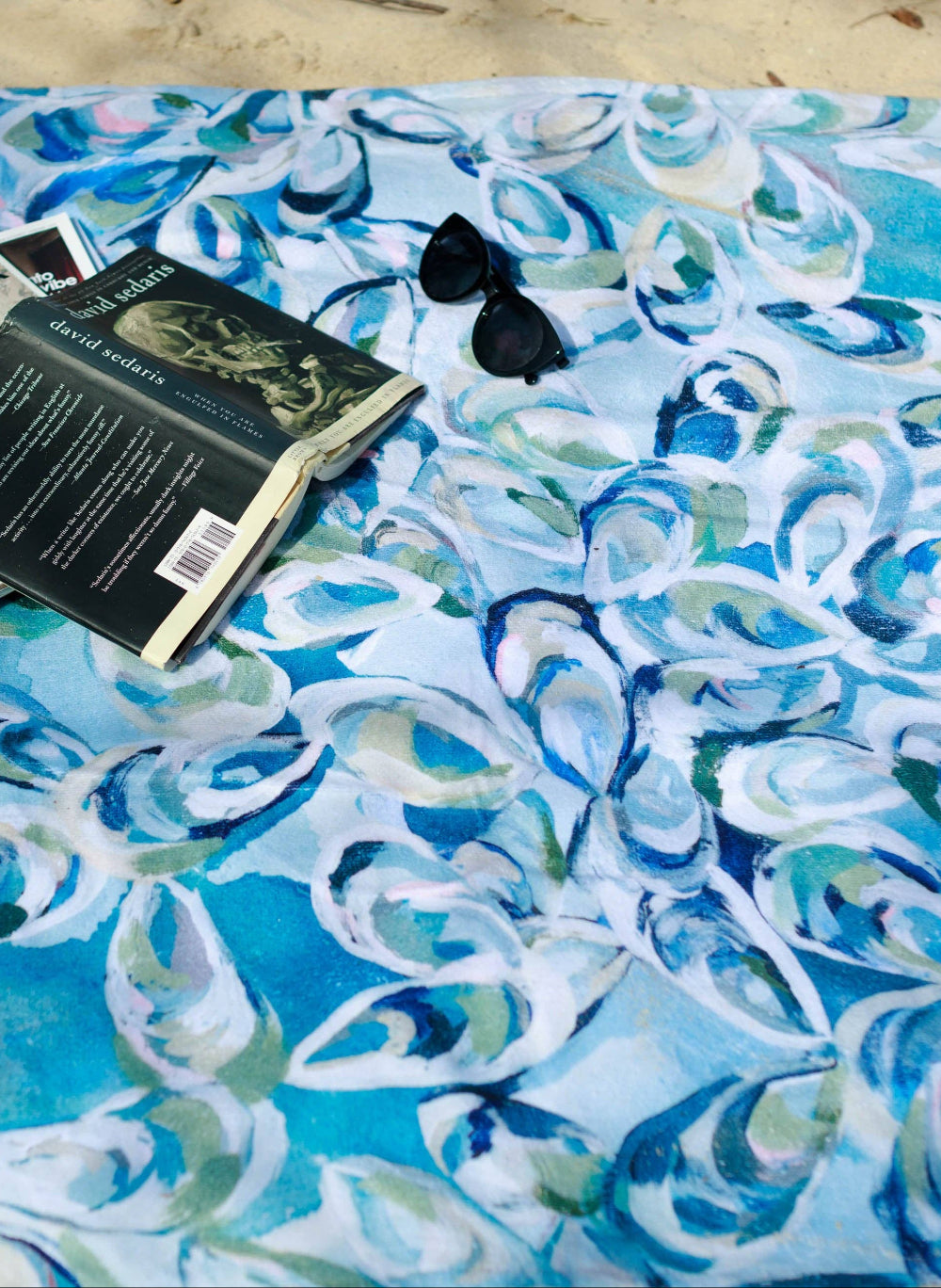 Blue and white oyster shell patterned towel with a book and sunglasses on top