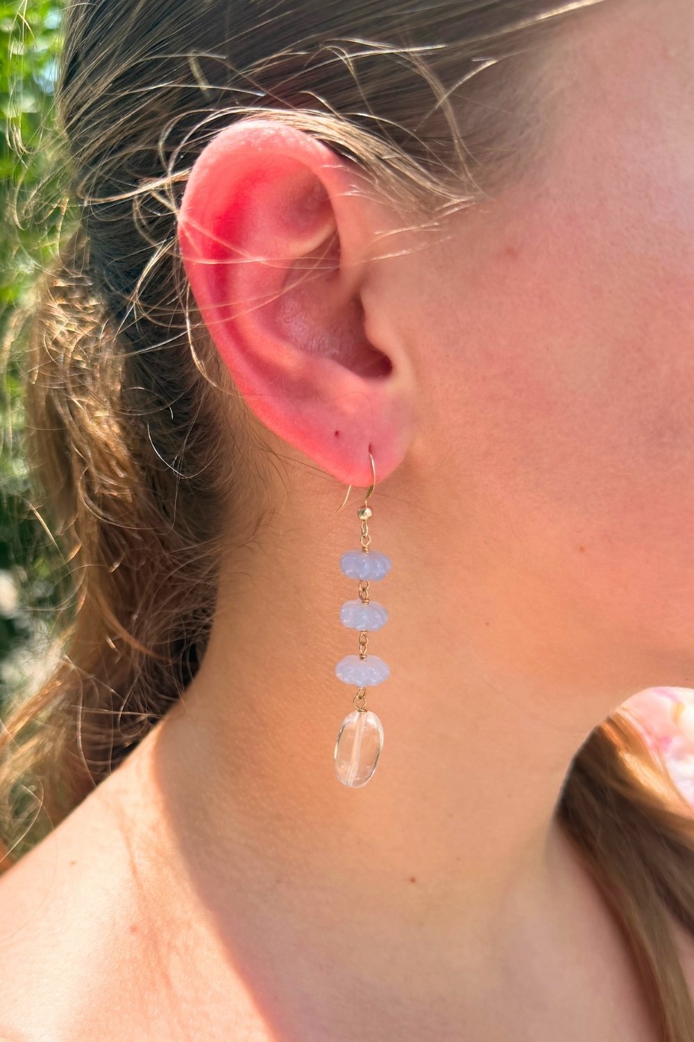 Close-up of a person wearing a bluebell dangling earring with clear and light blue stones.