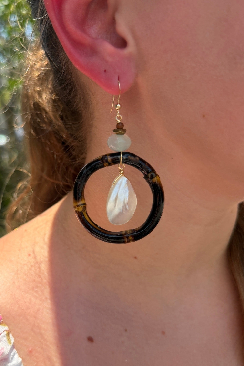 Calypso earring with a wood hoop and white teardrop pendant worn by a person outdoors