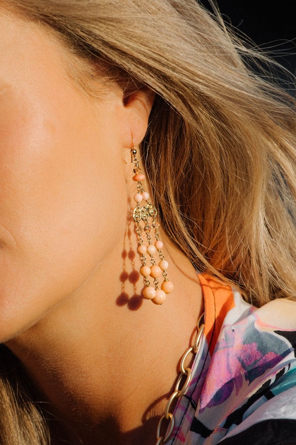 Close-up of a person wearing a coral chandelier earring with beads.