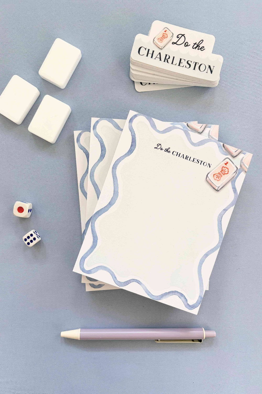 Stack of cards with 'Do the Charleston' text, dice, and a pen on a light blue background