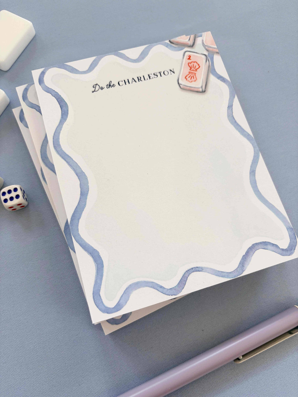 Notebook with decorative mahjong cover on a blue surface with dice and pen.