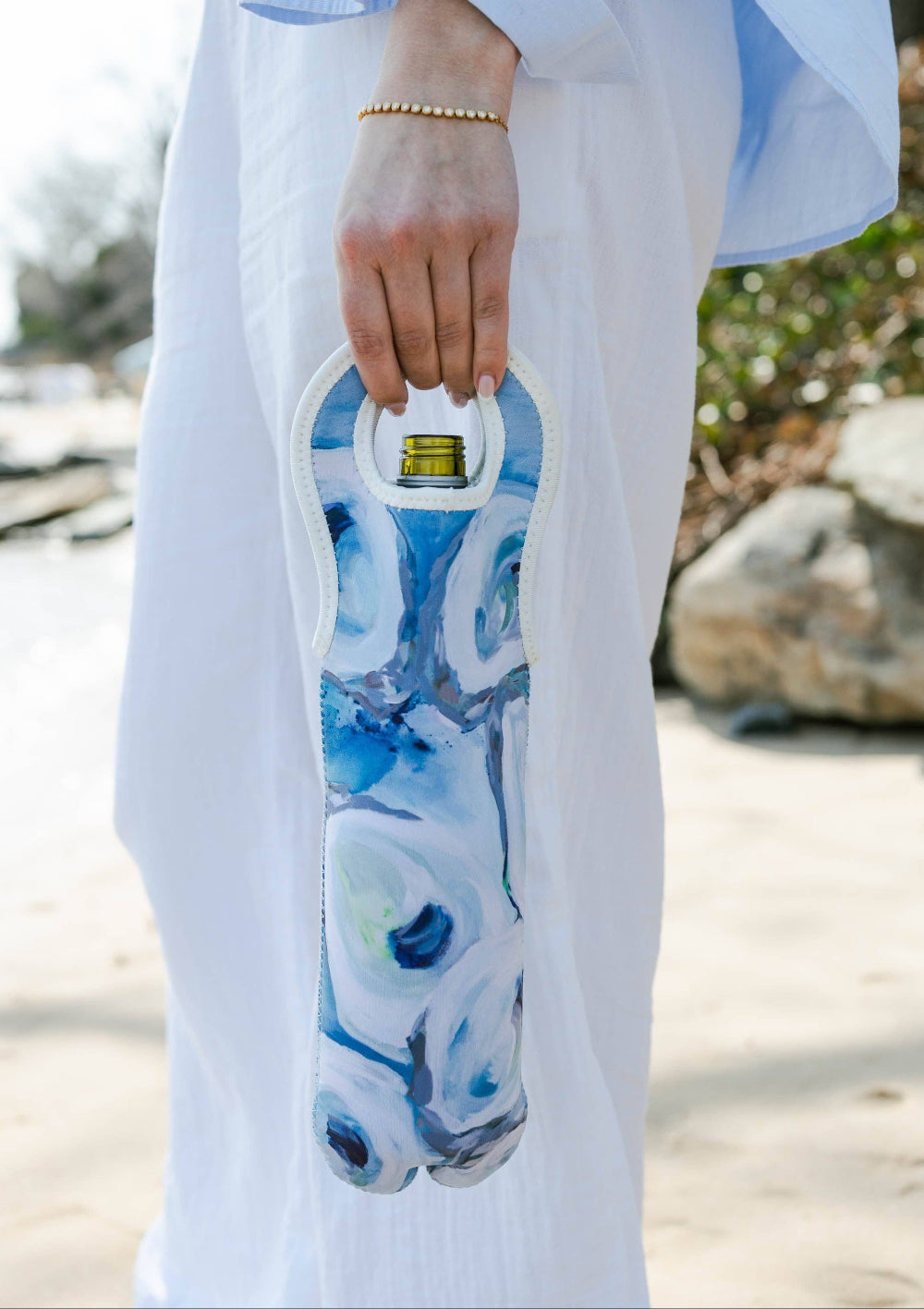 Person holding a blue and white oyster shell patterned wine tote with a blurred natural background