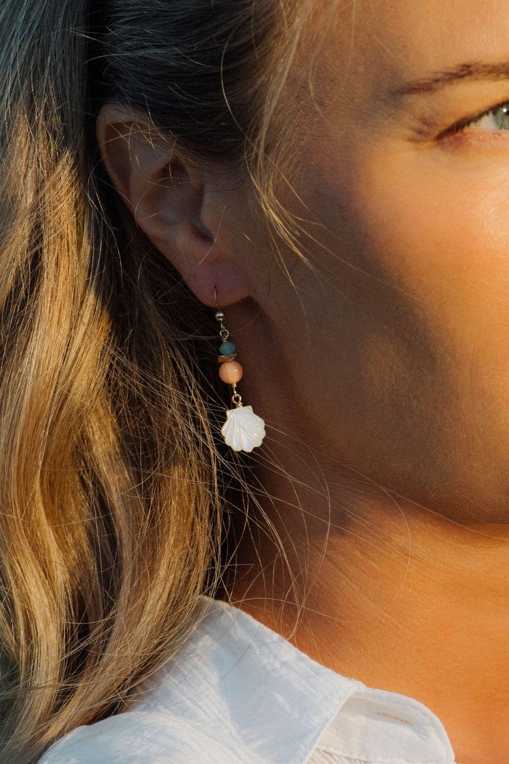 Close-up of a woman wearing a Golden Hour earring with a white shell design.