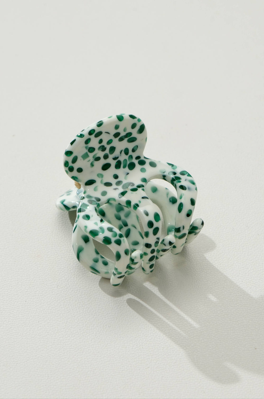 Green and white polka dot hair clip on a light gray background