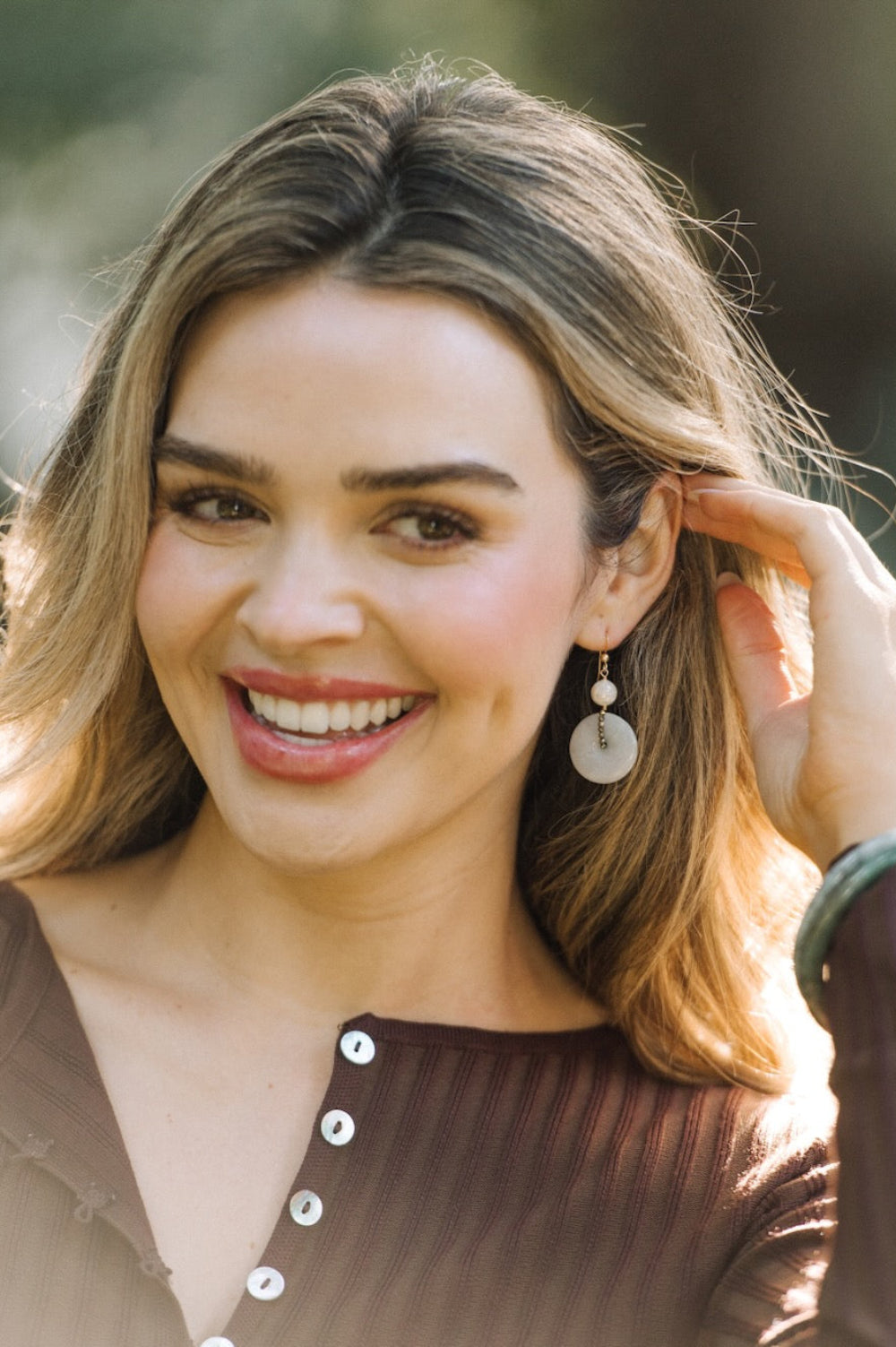 Woman with a smile, wearing earrings and a brown top outdoors