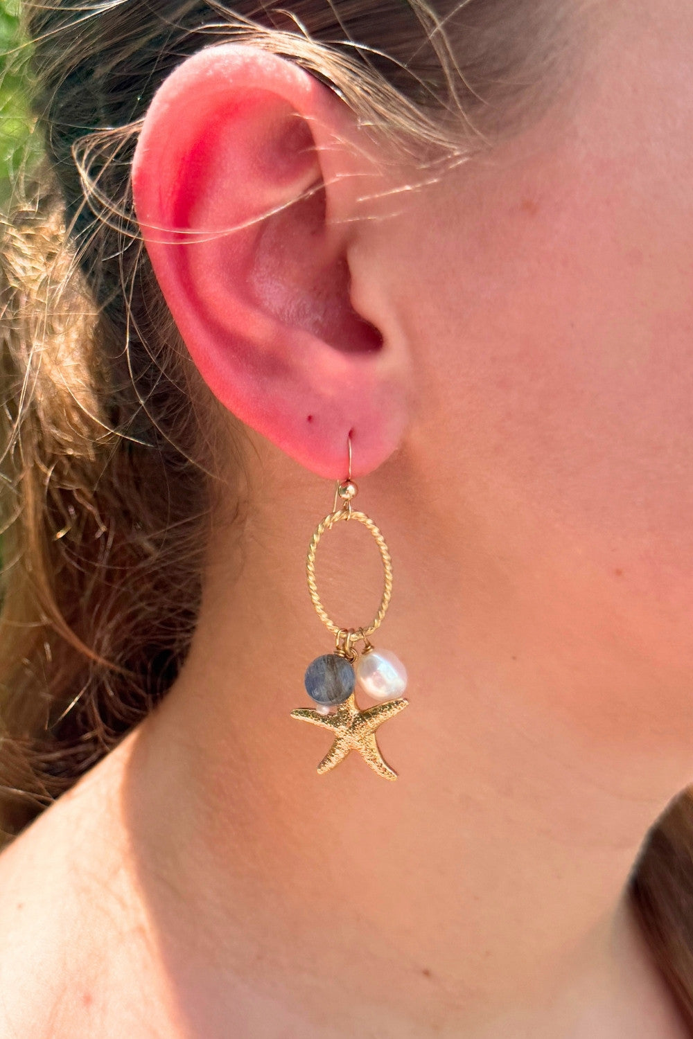 Close-up of an ear wearing indigo starfish gold earring with starfish and pearl charms.