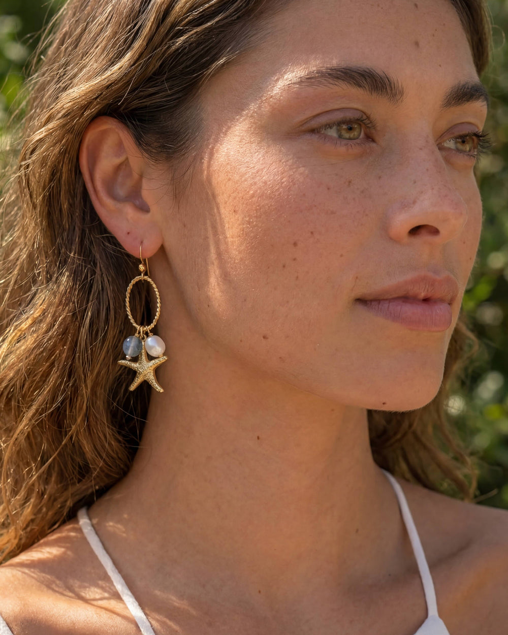 Woman wearing gold earrings with starfish and pearl design outdoors