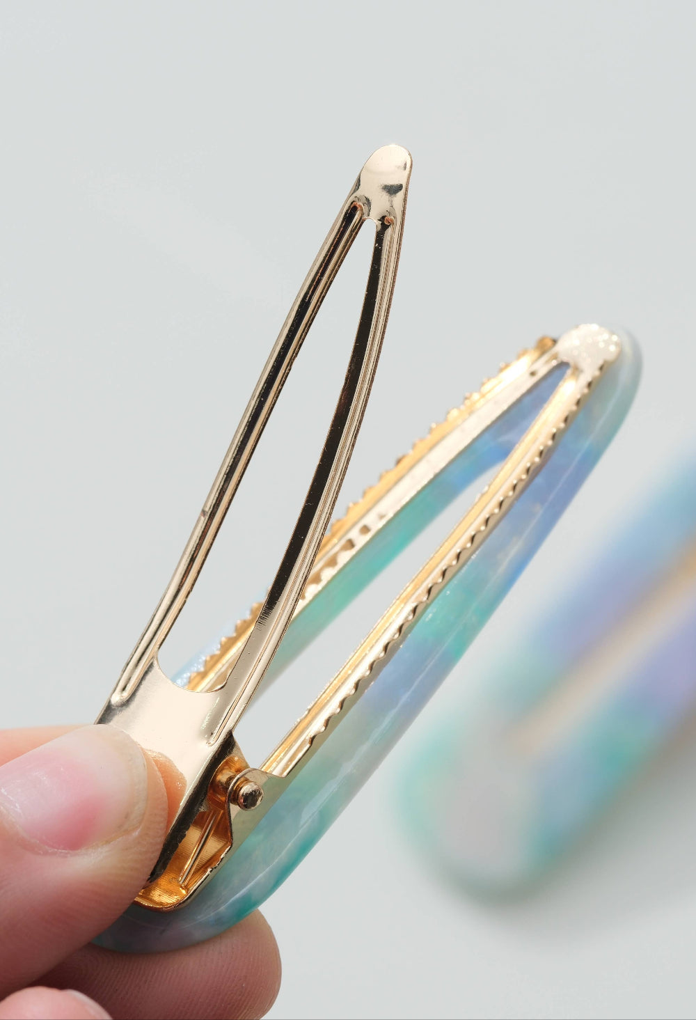 Gold hair clip held by a hand with a blurred colorful object in the background