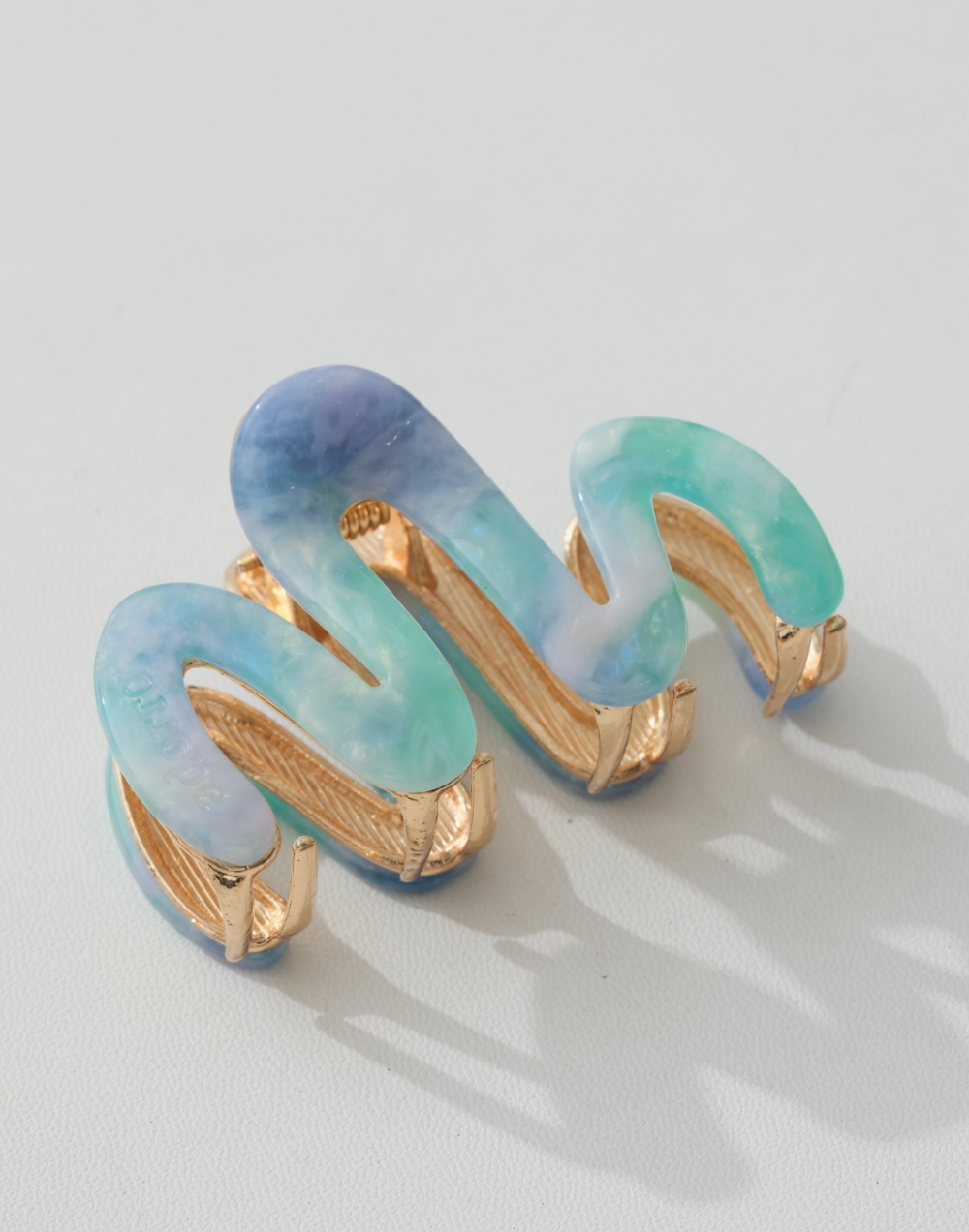claw clip with gold accents and pastel blue and green colors on a light gray background
